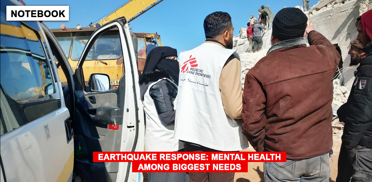 Two members of an MSF team stand and discuss with a person outside the rubble of a building.