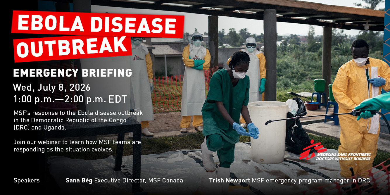 A member of MSF staff wearing personal protective equipment, carries mattresses between the white canvas structures at the new Ebola treatment center at the Elikya Hospital in Bunia.